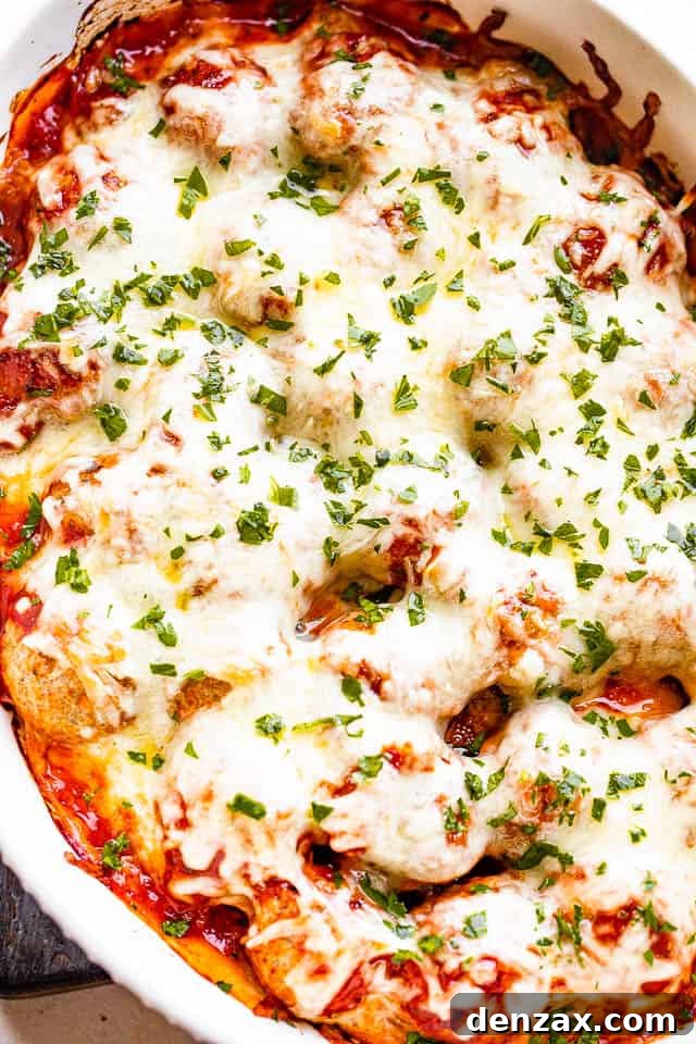 A close-up of a white baking dish filled with Cheesy Baked Meatball Casserole, featuring succulent meatballs completely blanketed in bubbly, melted mozzarella cheese and rich marinara sauce, fresh out of the oven.