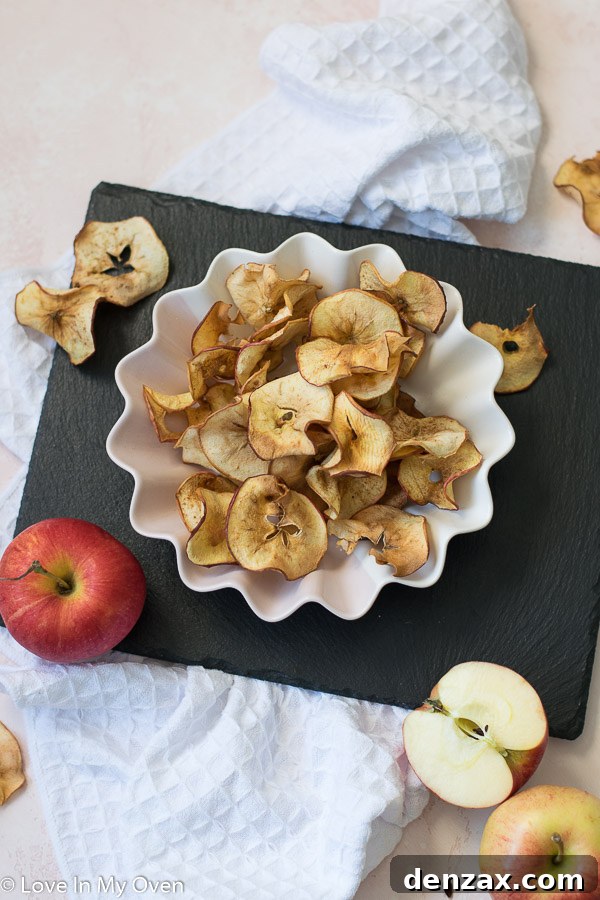 A bowl of freshly made crispy air fryer apple chips with a whole apple next to it
