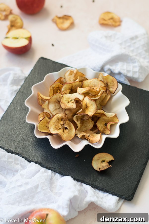 A large bowl of crispy air fryer apple chips, with two whole red apples beside it