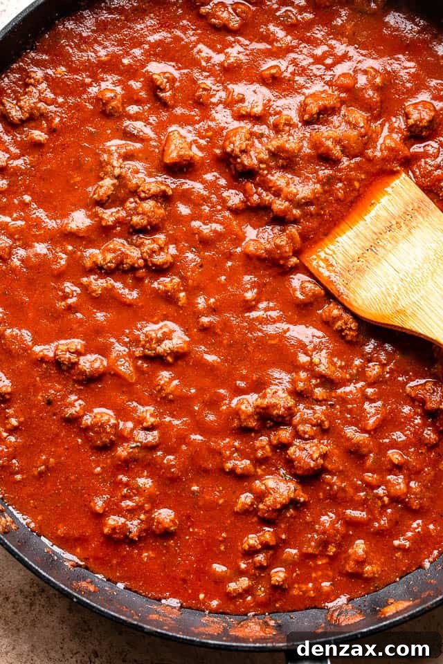 Preparing a rich ground beef and tomato sauce in a large black skillet, with fragrant herbs simmering.