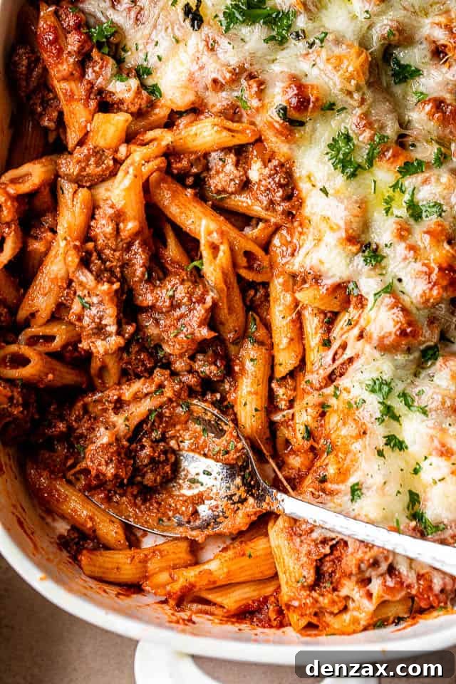 A large white baking dish filled with a golden, bubbly baked ziti casserole, garnished with fresh herbs, ready to be served.
