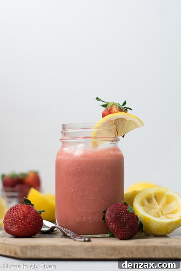 Vibrant homemade strawberry lemon curd in a clear glass jar, with fresh strawberries and lemon slices around it on a rustic wooden surface.