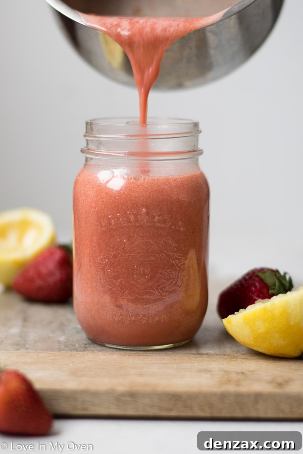 A close-up of smooth, creamy strawberry lemon curd in a glass bowl, with a small silver spoon resting in it.