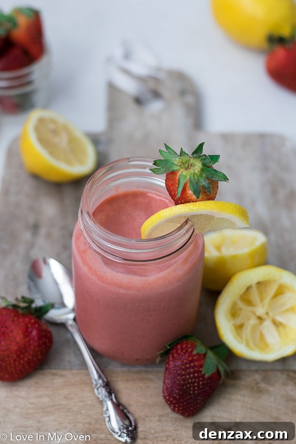 Two jars of homemade strawberry lemon curd on a rustic wooden board, garnished with fresh mint leaves, strawberries, and lemon slices.