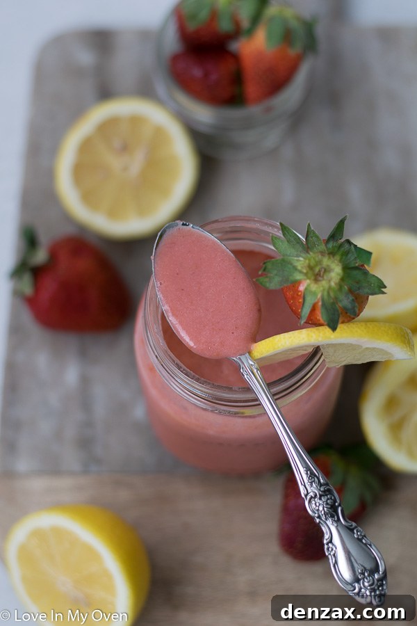 Homemade strawberry lemon curd in a clear glass jar, with a spoonful of curd in a small white dish, garnished with a mint leaf.