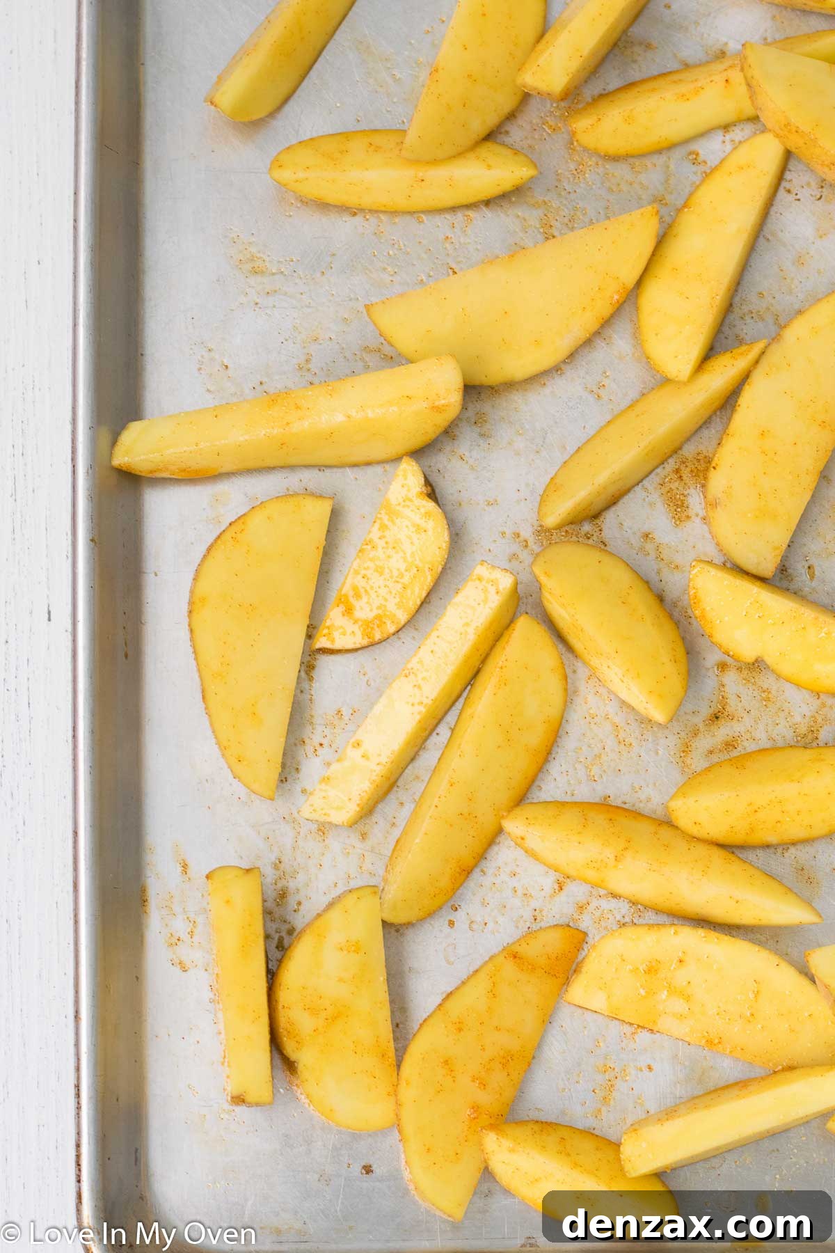 Potato wedges seasoned and ready for roasting, alongside a bowl of seasoning mix.