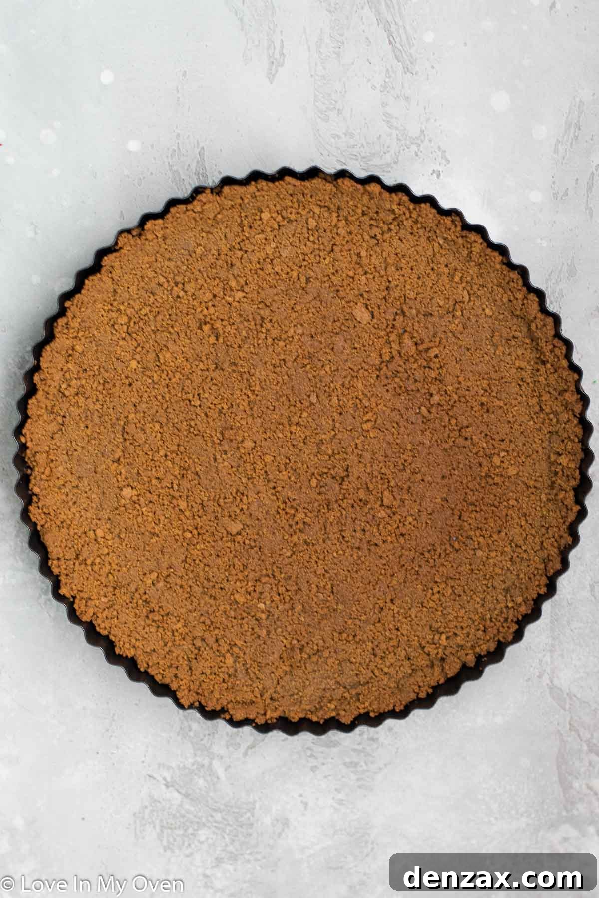 Gingersnap crust being pressed into a tart pan, forming an even layer.