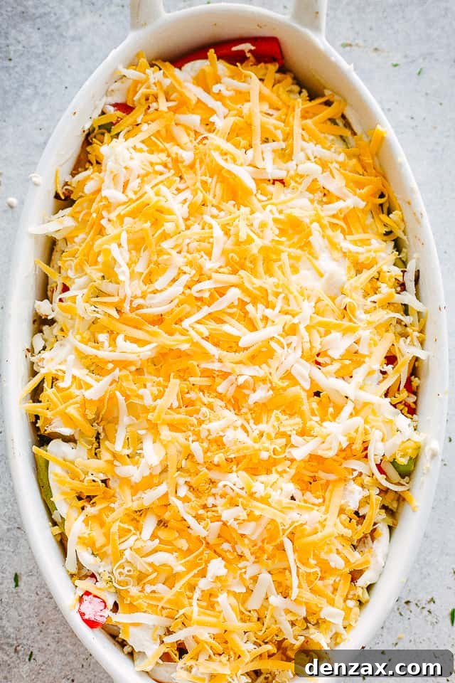 shredded cheese sprinkled over chicken and peppers in a white oval baking dish