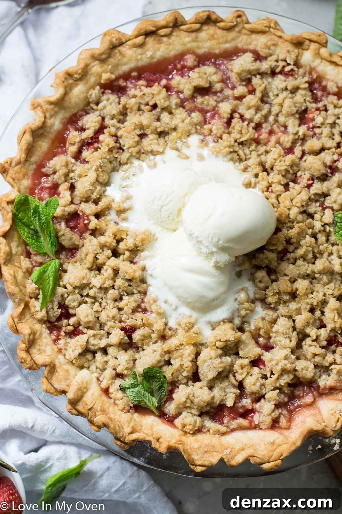 A slice of strawberry rhubarb crumble pie on a plate with vanilla ice cream