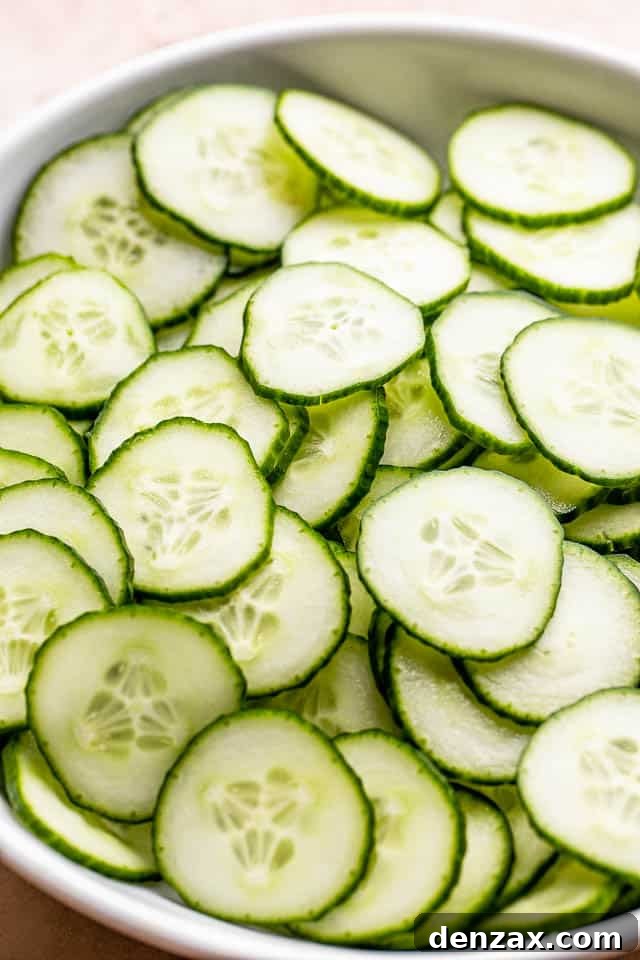 Freshly sliced cucumbers in a crisp white bowl, ready to be dressed for a healthy and refreshing salad.