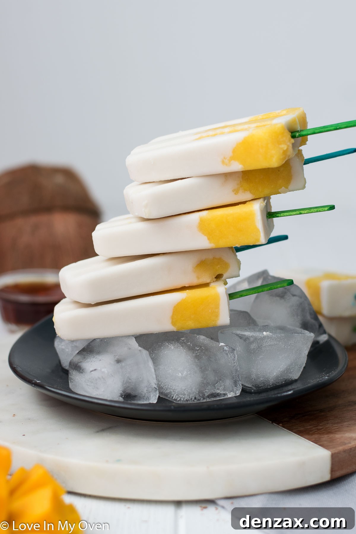 Two mango coconut popsicles on a wooden board
