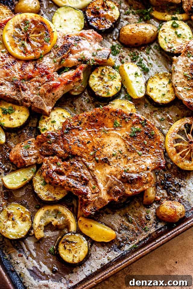 Another enticing view of the sheet pan, laden with golden baked pork chops and beautifully roasted squash, potatoes, and vibrant lemon slices, showcasing a complete and appetizing meal.