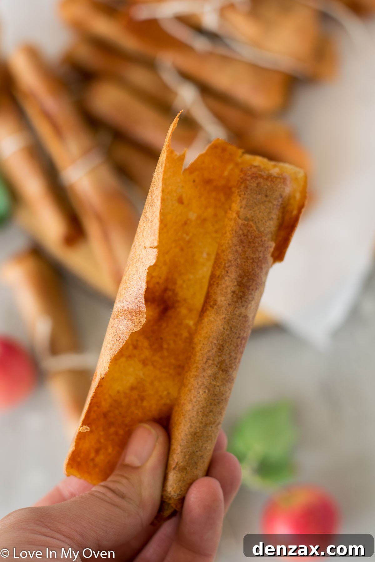 Homemade apple fruit leather being rolled up from the parchment paper, showcasing its flexible texture