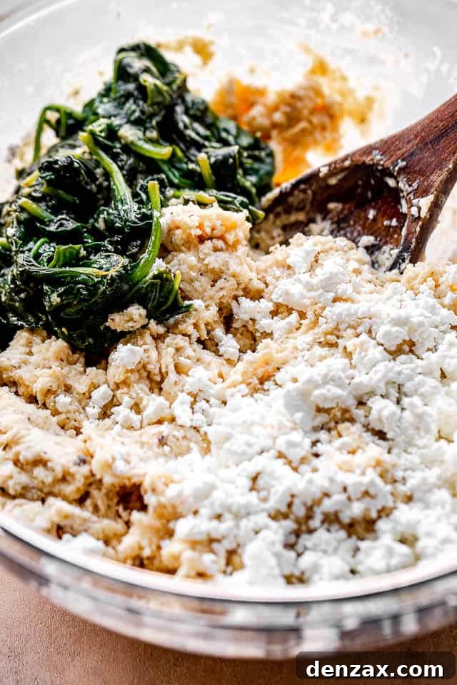 Side view of a large mixing bowl, showing spinach, crumbled feta cheese, and flour being combined to create the no-yeast bread batter.