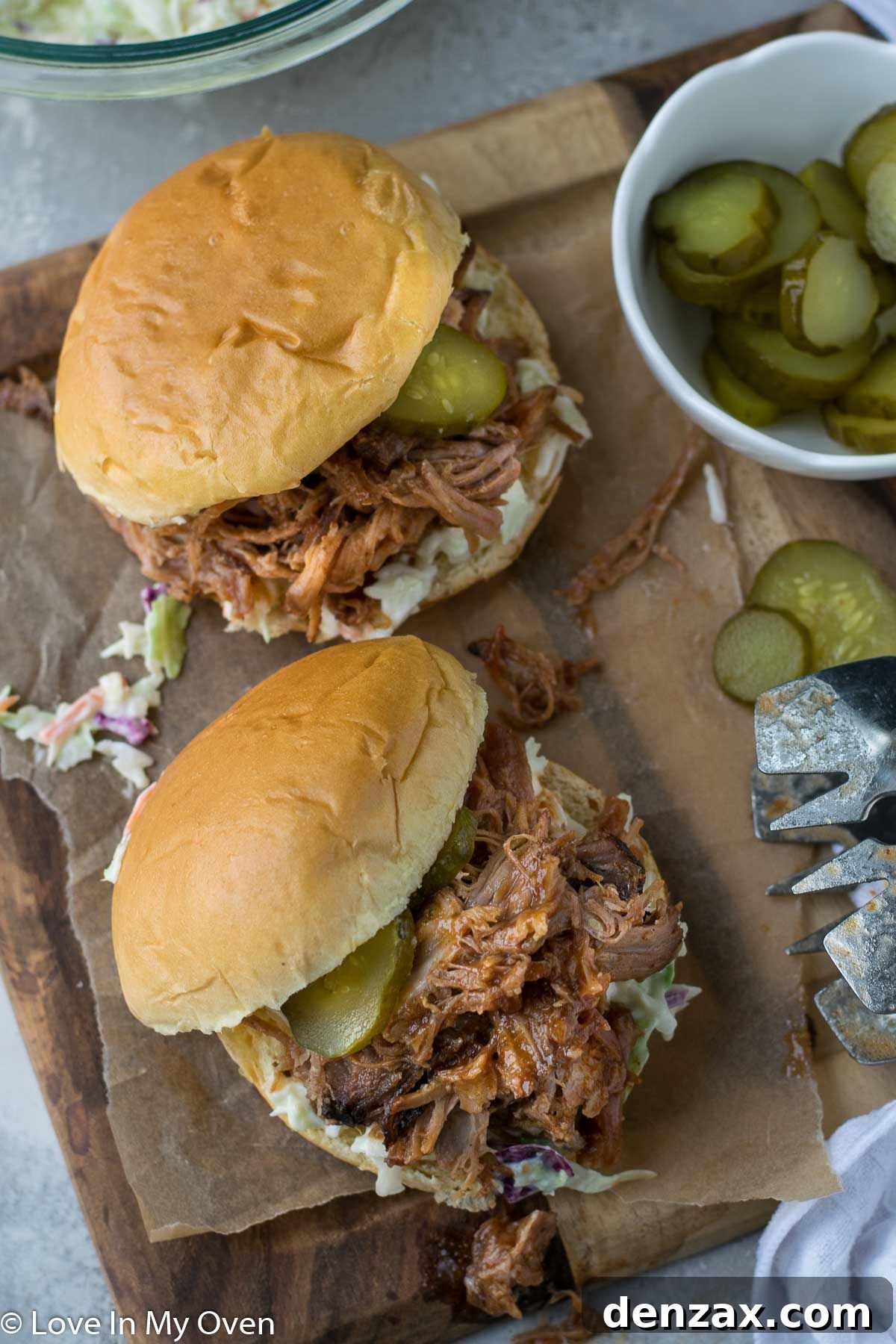 A slider bun filled with apple cider pulled pork, coleslaw, and a pickle.