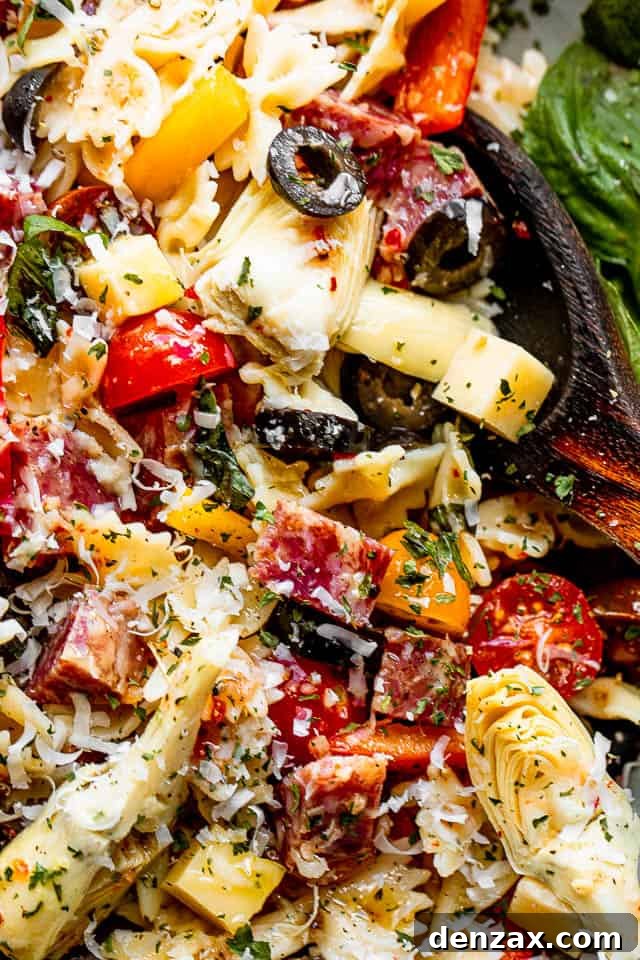 close up shot of a salad bowl filled with pasta, cheese cubes, salami cubes, tomatoes, and olives, showcasing the vibrant ingredients