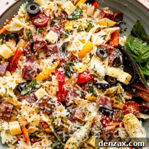 top view shot of a wooden spoon in a bowl filled with pasta, cheese cubes, salami cubes, tomatoes, and olives