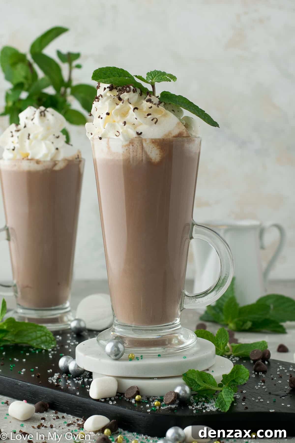 Two mugs of mint hot chocolate, one with whipped cream and the other with marshmallows, on a rustic surface.