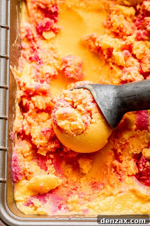 Close-up shot of mango strawberry frozen yogurt in a loaf pan with an ice cream scoop, ready to be served