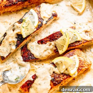 white pan with four salmon fillets topped with lemon slices and cream sauce