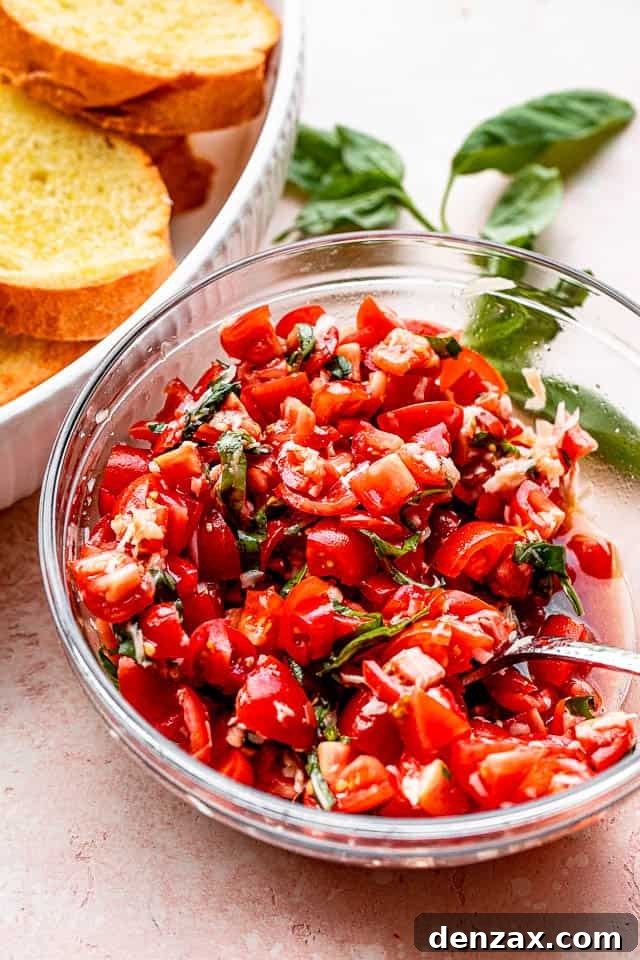 A vibrant tomato and basil salad, freshly mixed in a bowl, sits beside golden-brown toasted garlic bread slices on a pristine white surface, ready for assembly.