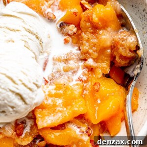 silver spoon inside a white bowl filled with a Peach Dump Cake and a scoop of ice cream