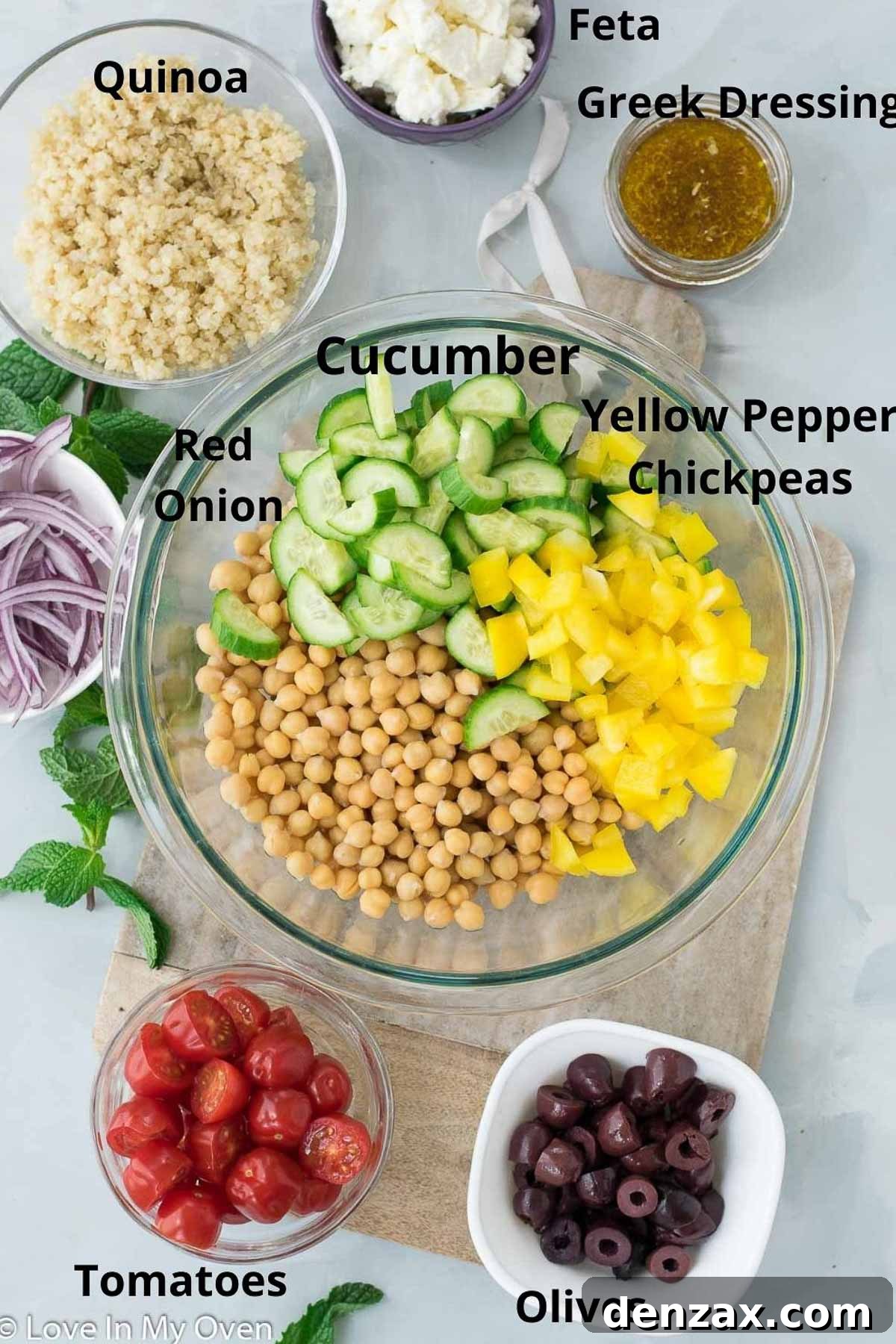 Fresh ingredients laid out for Greek Chickpea Salad: chickpeas, quinoa, vegetables, feta, and mint.