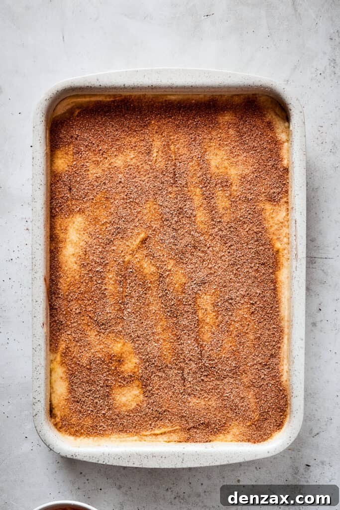 A baking dish with cheesecake filling and crescent roll crusts, topped with butter and cinnamon sugar.