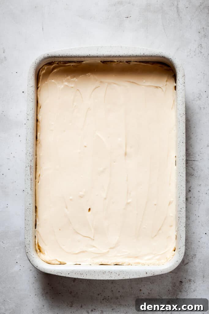 A baking dish with dough on the bottom and cream cheese filling spread in an even layer.