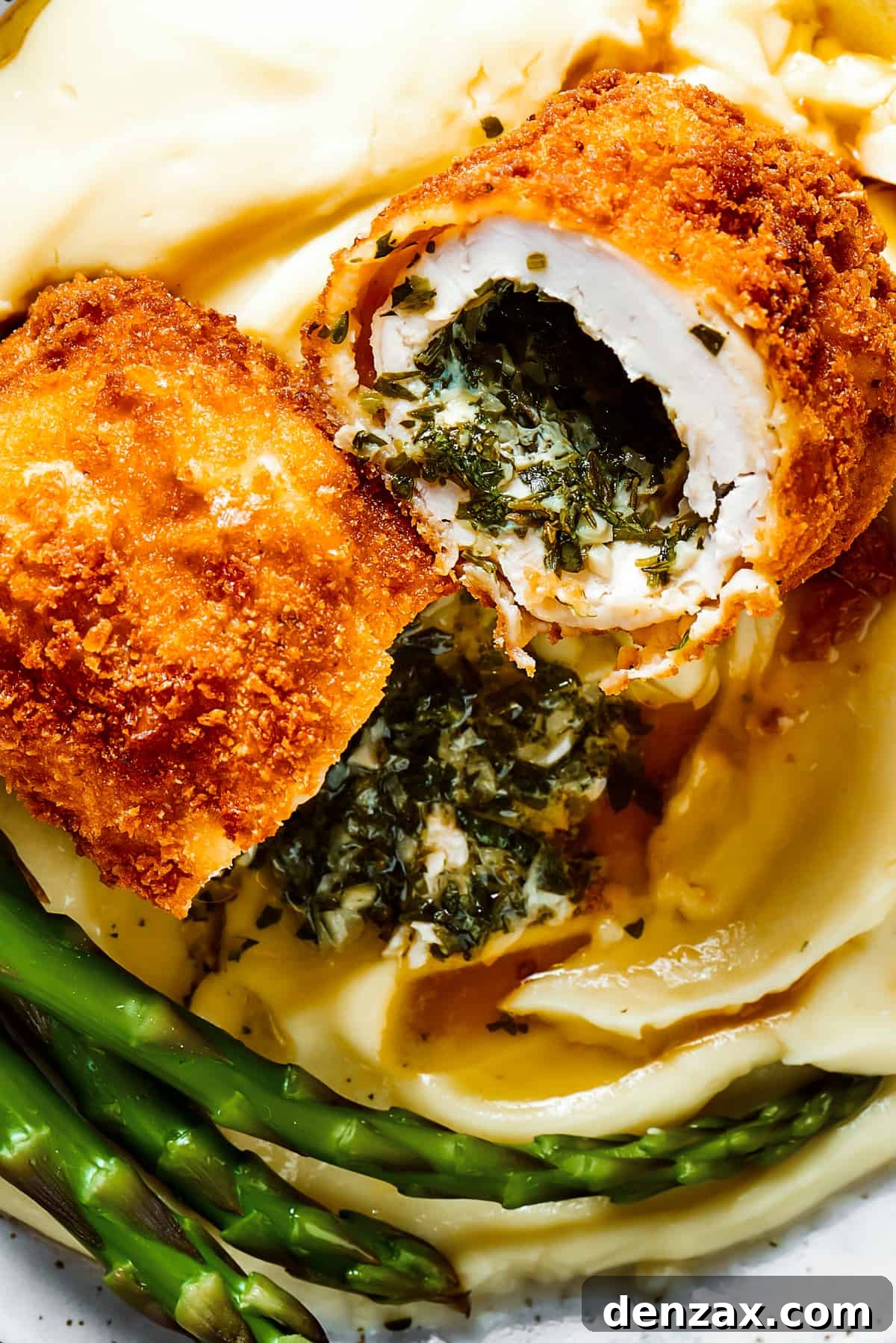 A serving of chicken Kiev cut in half to show the buttery filling, alongside mashed potatoes and asparagus.