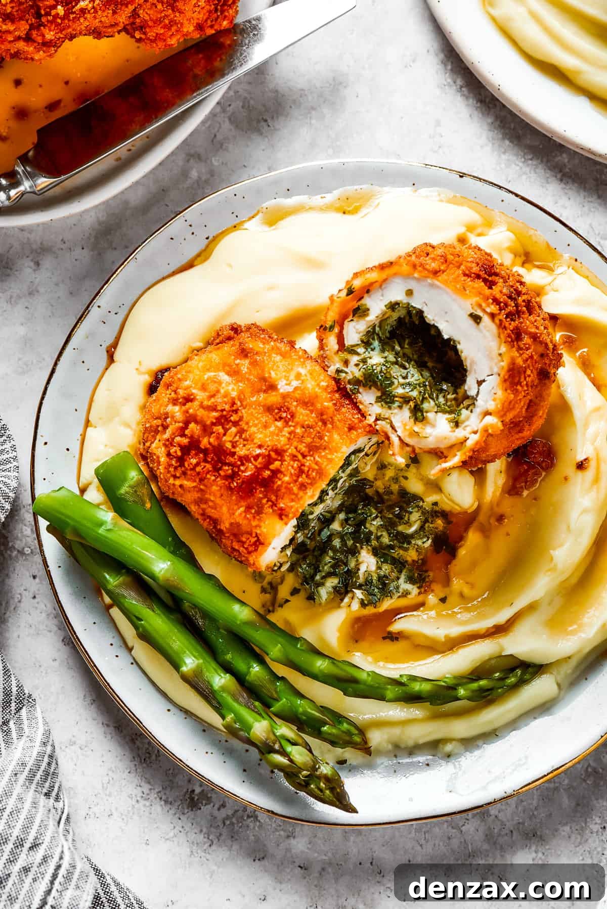 A serving of mashed potatoes and asparagus with chicken Kiev cut in half to show the buttery filling, ready to be enjoyed.