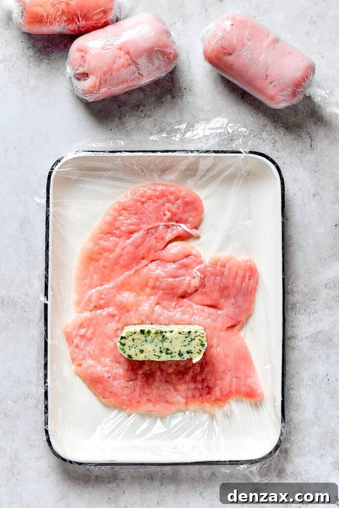 A slice of compound butter placed on a butterflied chicken breast, ready to be rolled.