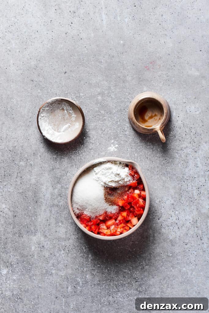 A small saucepan with chopped strawberries, sugar, and cornstarch being mixed and cooked on a stove.