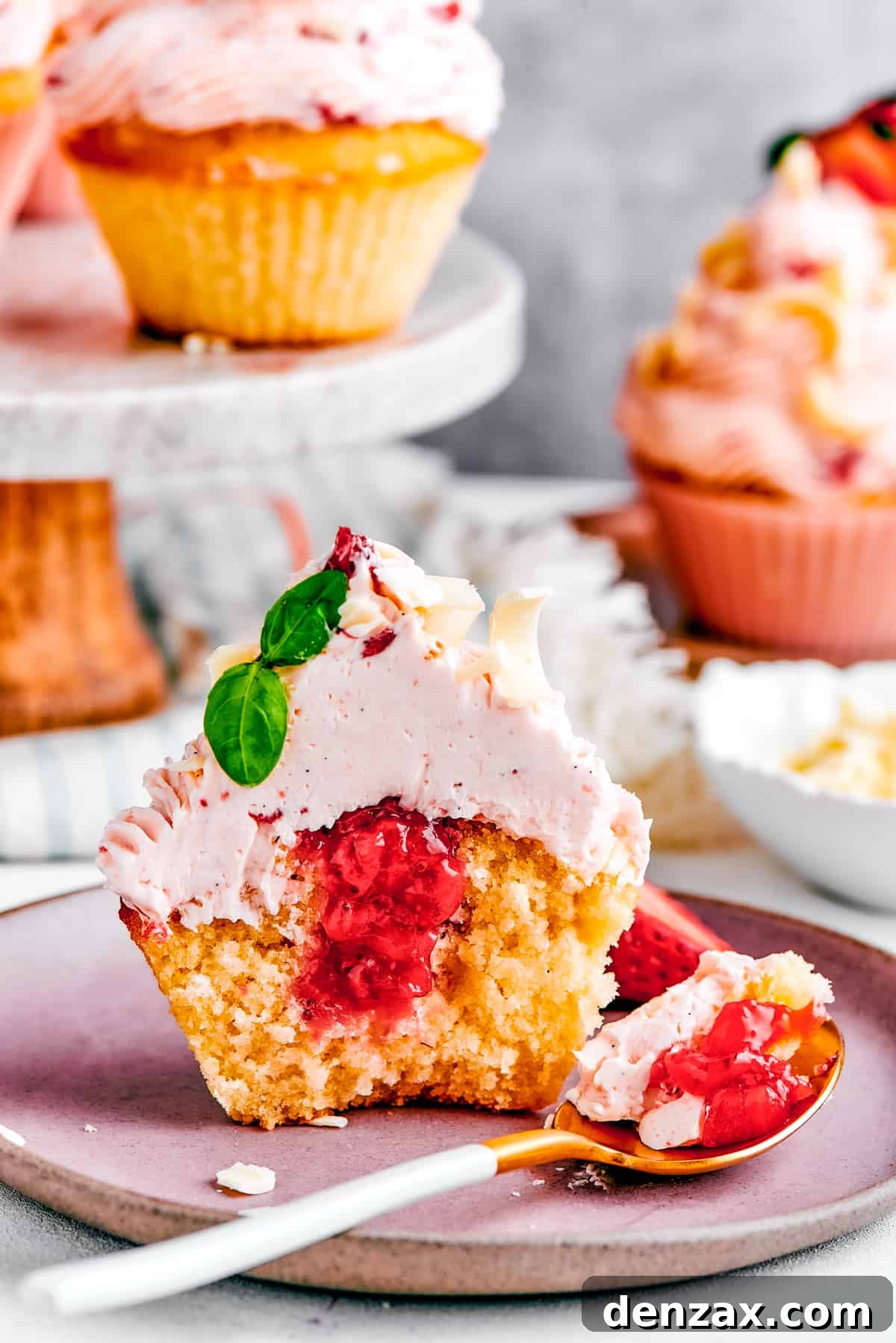 A strawberry cupcake on a white plate, cut in half to showcase the luscious strawberry filling inside.