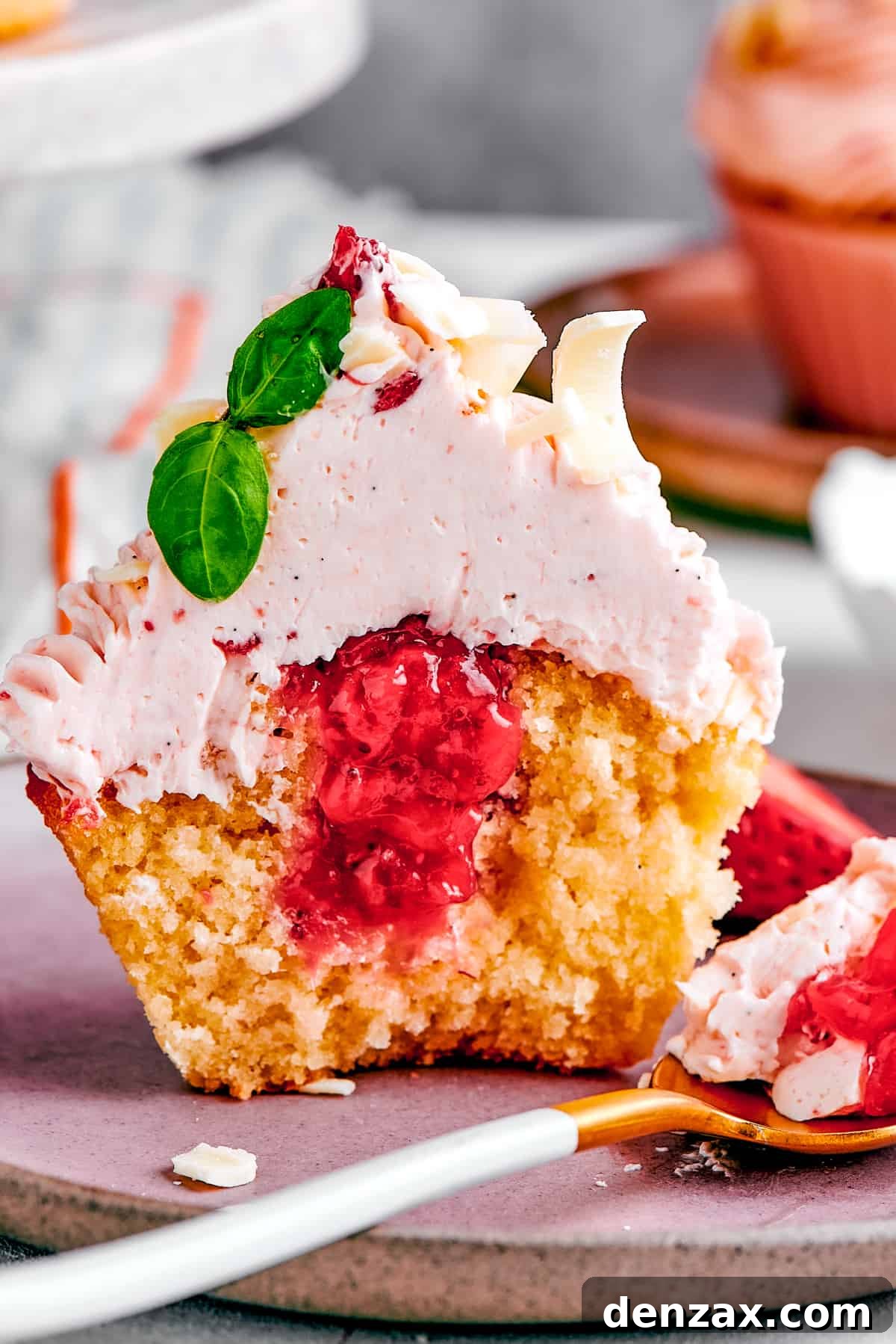 A strawberry cupcake, perfectly cut in half to reveal its vibrant strawberry filling nestled within the tender cake.