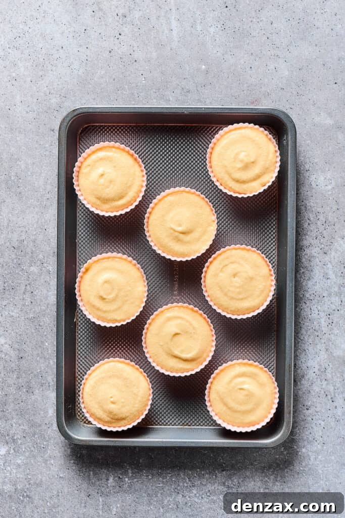 A baking tray filled with unbaked cupcakes, neatly portioned into liners, ready for the oven.
