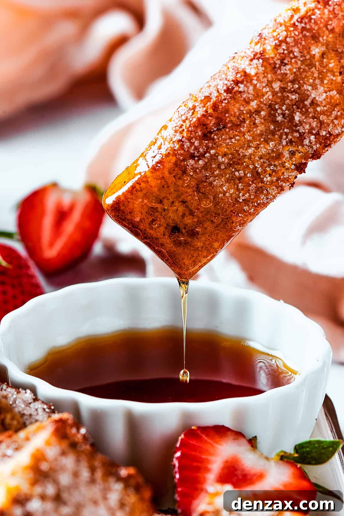 Lifting a piece of toast from a cup of syrup, with the syrup dripping back into the cup.