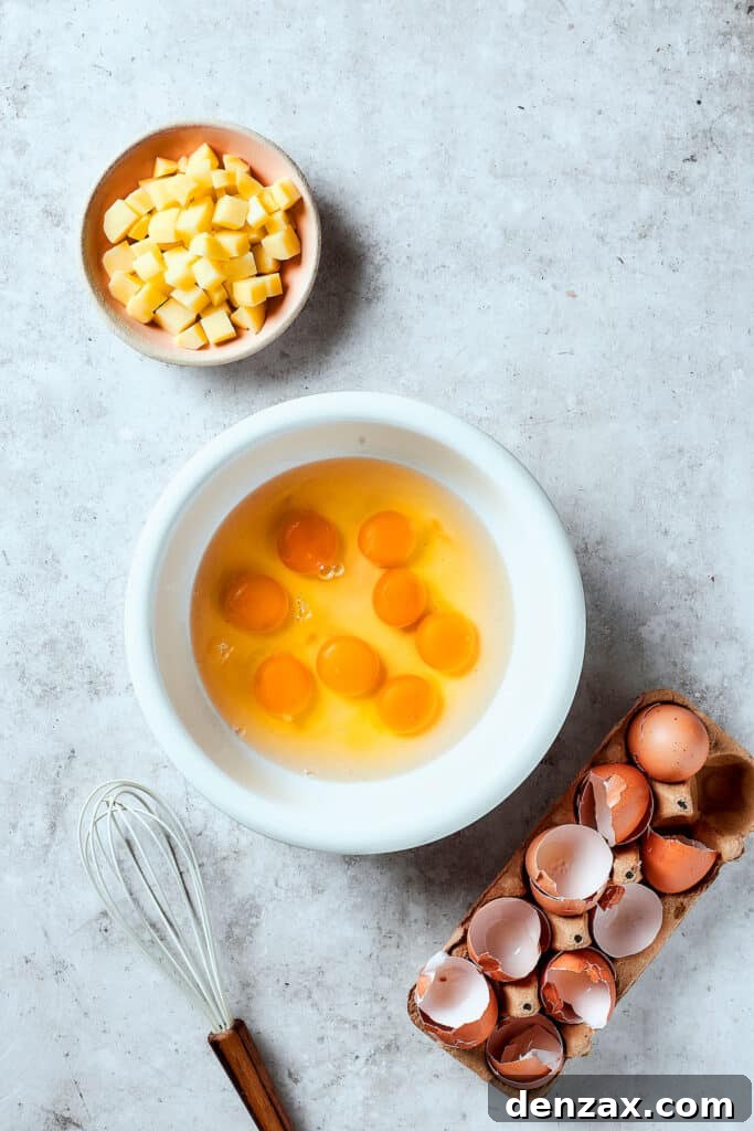 Fresh eggs cracked into a mixing bowl, ready to be whisked, with a bowl of cooked potatoes nearby on a rustic kitchen counter.