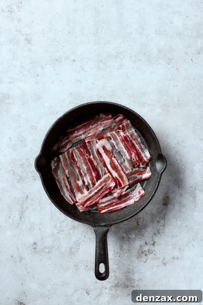 Close-up of bacon frying in a hot cast-iron skillet, sizzling and crisping up, ready to add savory depth to the frittata.