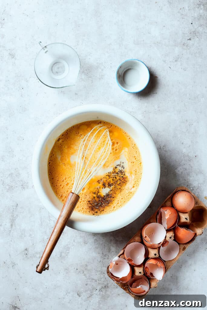 A bowl of whisked eggs being seasoned with salt, pepper, and milk, creating the creamy base for the frittata.