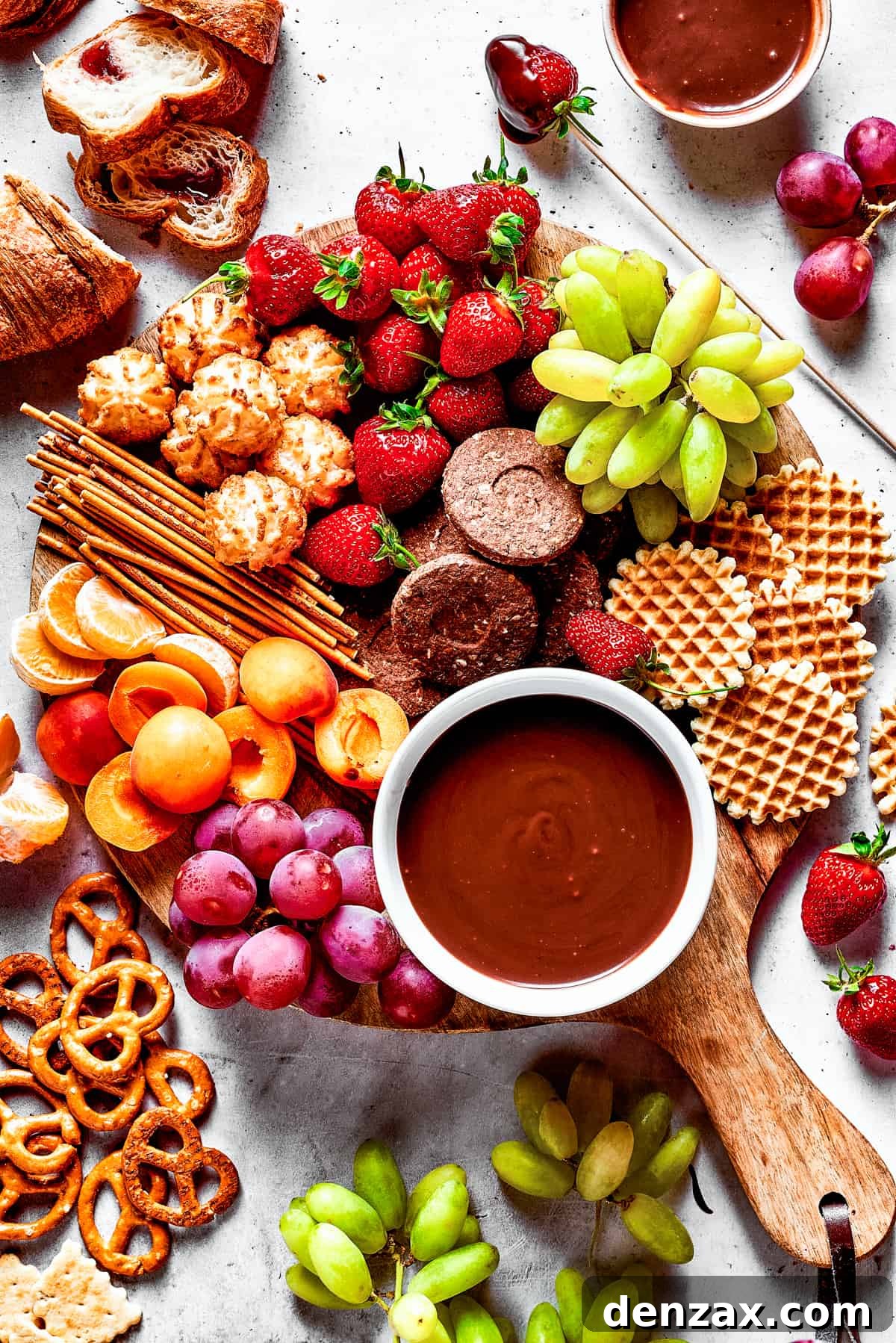 A dessert board with fruit, waffles, pretzels, and with a bowl of fondue in the center.