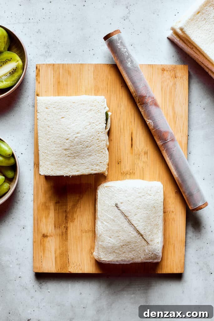 Hands meticulously wrapping a completed fruit sandwich in plastic wrap.