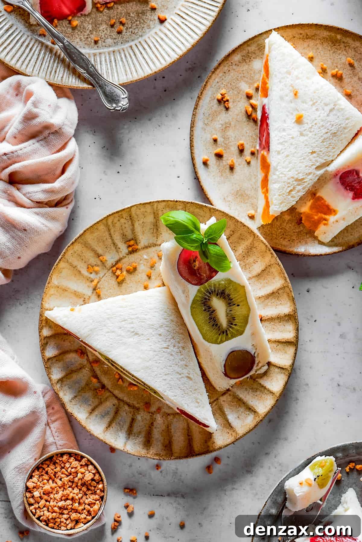 Multiple fruit sandwiches, each cut diagonally, arranged on small, decorative plates, ready to be served.