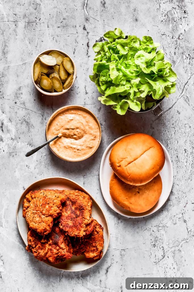 All the components for assembling the chicken sandwich: pickles, lettuce, spicy mayo, buns, and fried chicken.