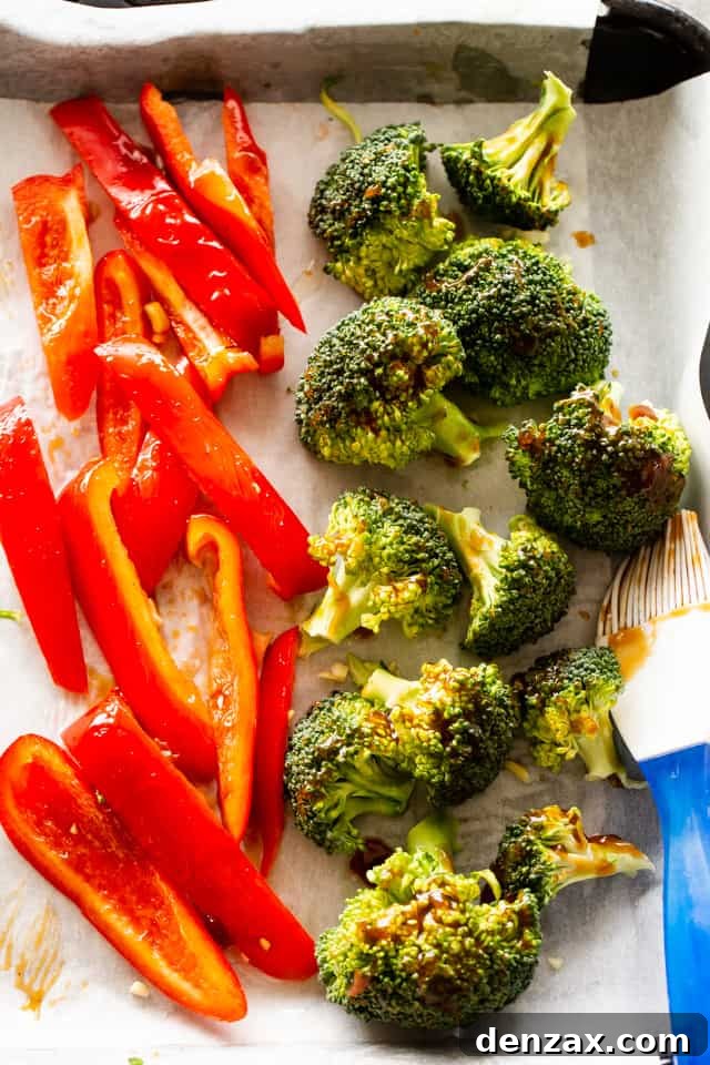 Red bell pepper slices and broccoli florets arranged on a baking sheet, glistening, ready for roasting.