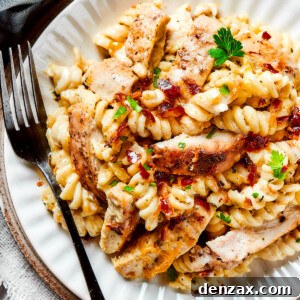 A dinner plate of pasta and chicken with creamy sauce and bacon.