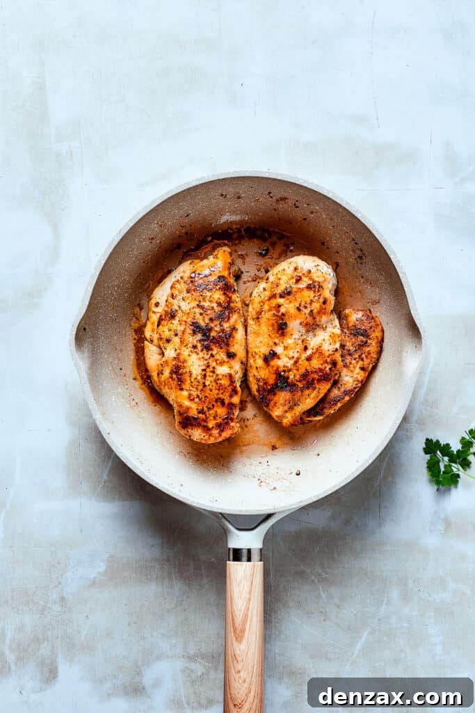 Cooking seasoned chicken breasts in a large skillet, browning beautifully.
