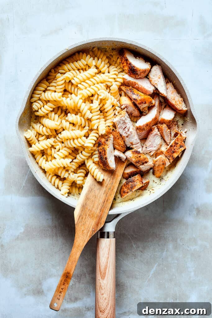 Adding perfectly cooked chicken and pasta to the creamy sauce in a skillet, stirring to combine.