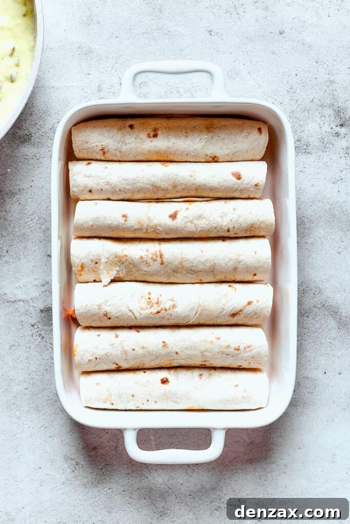 A baking dish full of rolled-up enchiladas, neatly arranged before saucing.