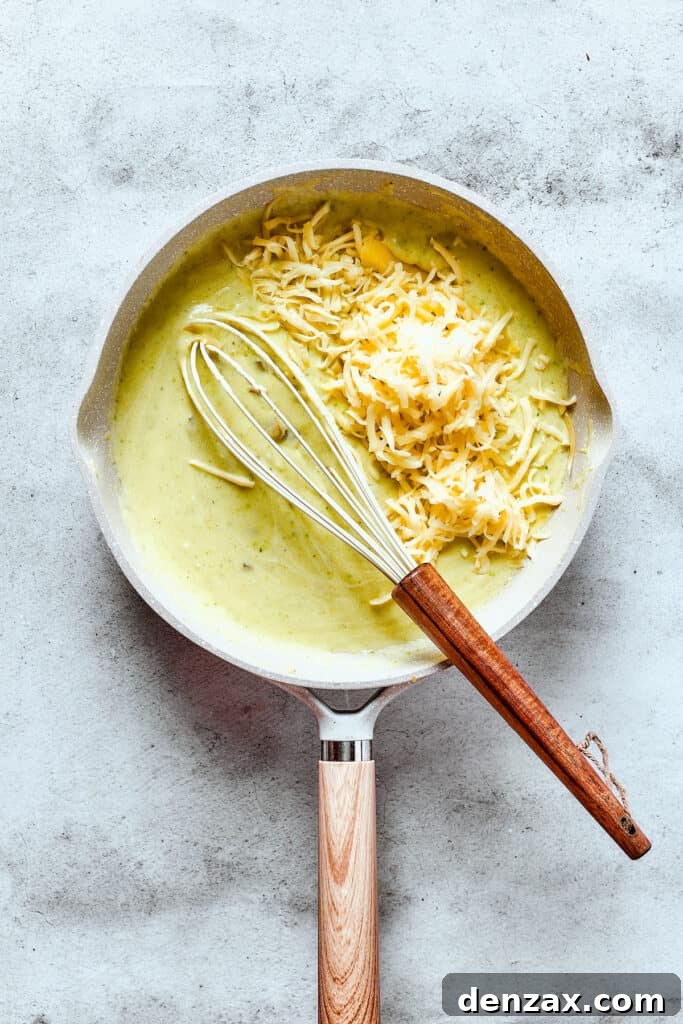 Whisking cheese into a creamy enchilada sauce in a saucepan.